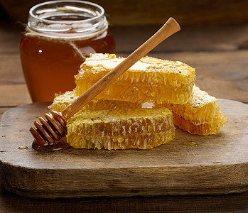 在一罐蜂蜜后面的木板上加蜂蜜的蜡蜂窝食物勺子黄色甜点液体木头棕色营养桌子玻璃图片