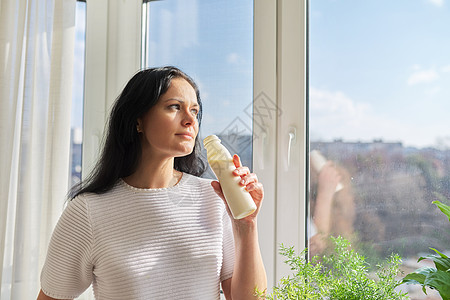 女人从站在窗边的瓶子里喝牛奶饮料 牛奶酸奶乳品健康饮料细菌生活维生素食物女性早餐女士成人产品中年图片