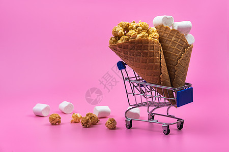 有冰淇淋甜食和粉红背景糖果的购物车消费者销售锥体购物商业爆米花小吃食物零售市场图片