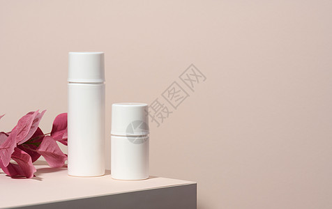 两根白色的化妆品塑料管 放在一个木制讲台上 背面有阴影的蜜蜂背景 奶油 香波和液体物质的容器背景图片