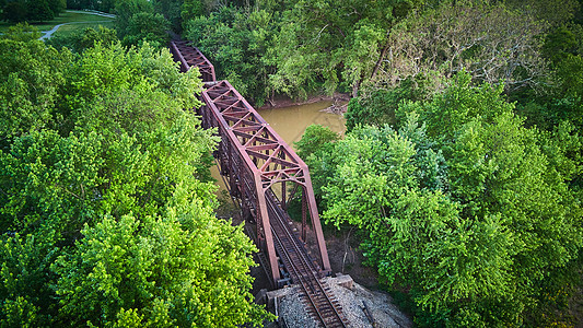 在大金属桥上空的空中观察 沿绿树环绕的河上铁轨背景图片