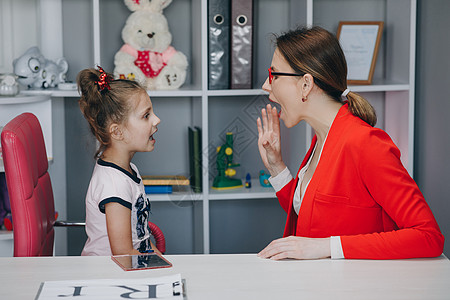 上学小女孩语言治疗师办公室的可爱小女孩 小孩子在家里的私人课程中与治疗师一起练习发音背景