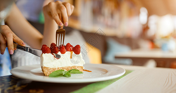 女人的手拿着一块草莓芝士蛋糕盘子 女孩的手用叉子切蛋糕背景图片