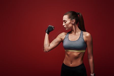 体育女运动员正在训练 用哑铃在红色背景上站立着的图片