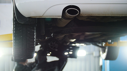 汽车服务 — 机械师在提升的排气管下工作时拧开汽车装置图片