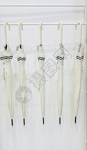五把米色伞挂在衣钩钩上 白色背景 为雨季做好准备 五把现代雨伞挂在挂在白色衣架上的架子上图片