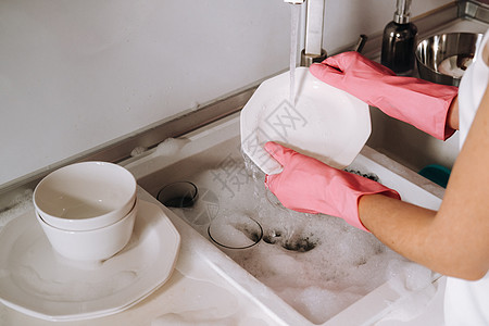 戴粉红色手套的家庭主妇女孩用洗涤剂在水槽里用手洗碗 女孩在家里打扫房子 戴着手套洗碗脸盆洗涤家务菜肴公寓漂洗卫生餐具洗衣机眼镜图片