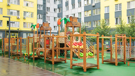 一个高层建筑的庭院 在一个没有人的雨天 有一个由木头和塑料制成的现代大型游乐场 空荡荡的户外游乐场 儿童游戏和运动的场所剧场梯子图片