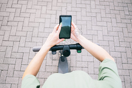 女性在用电子摩托车站着时使用智能手机的视角图片