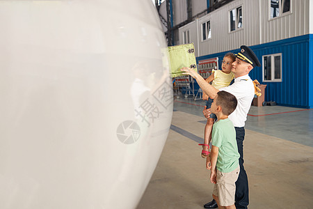 身着制服的专业飞行员向他的两个小孩展示飞机的部件 他们来飞机库看望他们的父亲图片