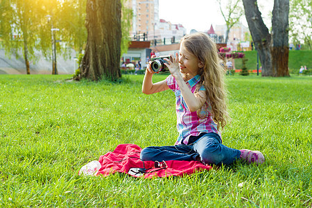 8岁的小女孩 看着摄像头坐在城市公园的绿草坪上图片