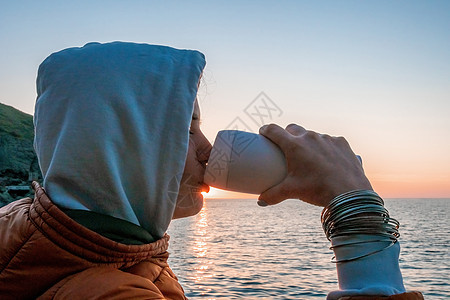 一位年轻的女游客拿着咖啡杯坐在户外享受日出海山景观 女性瑜伽健身程序 健康的生活方式 和谐与冥想日落海滩自由假期海洋山脉旅行杯子背景图片