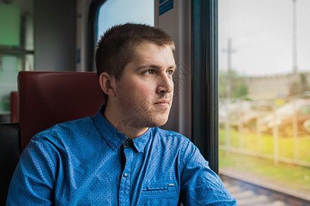 穿蓝衬衫的年轻欧洲人 从现代电动列车行驶的窗外图片