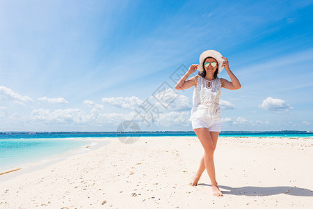 在海滩上戴着帽子的美丽笑脸女孩旅行女士享受女性头发闲暇太阳海洋裙子天空图片