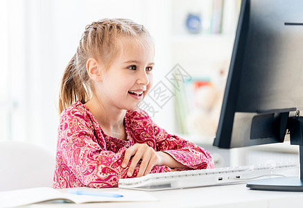 在电脑桌上微笑的小女孩在计算机台女儿孩子意义大学童年键盘电脑瞳孔学校房间图片