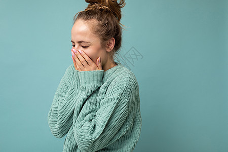 年轻笑着的正面漂亮迷人的金发女人的画像 带着真诚的情感穿着时髦的蓝色毛衣 在蓝色背景中被隔离 有自由空间和遮住嘴巴图片