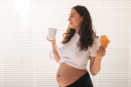 孕妇饮食在家带羊角面包的快乐孕妇 怀孕 吃东西和人的概念垃圾母性母亲腹部糕点婴儿盘子早餐甜点营养背景