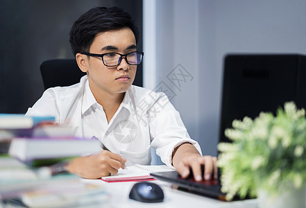 年轻人用笔记本笔记本学习和写笔记本学生技术商业笔记男性桌子电脑写作工作大学图片
