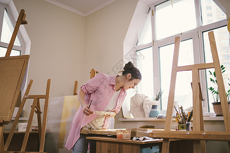 可爱的女人在艺术工作室的画布上作画 艺术家创作图片 艺术学校或工作室 使用颜料 画笔和画架 爱好和休闲的概念 工作区的女画家女性图片