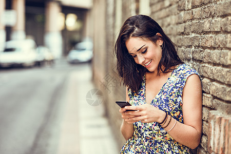 在户外使用智能手机微笑的年轻女子头发女性技术街道裙子卷发电话成人女孩棕色图片