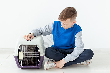 笑笑的男孩拿着一个笼子和一只苏格兰折叠猫坐在他旁边 坐在新公寓的地板上 保护宠物的概念小猫工作室折叠尾巴哺乳动物毛皮婴儿猫咪眼睛图片