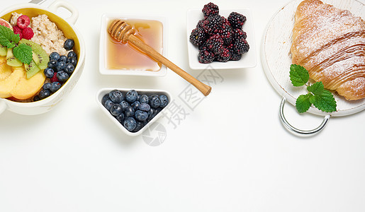 盘子里放着燕麦片和水果 半个成熟的橙子和鲜榨果汁放在透明玻璃瓶中 蜂蜜放在白桌上的碗里 健康早餐稀饭果汁谷物制品粮食羊角桌子小吃图片