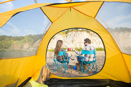 人民 旅游和自然概念     坐在黄色帐篷附近的可爱情侣女性微笑喜悦拥抱娱乐太阳镜黑发冒险爬坡男人图片