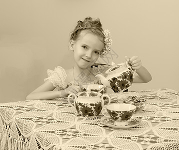 可爱的小女孩在旧桌边喝茶微笑食物青年裙子孩子女性派对孩子们幸福童年图片