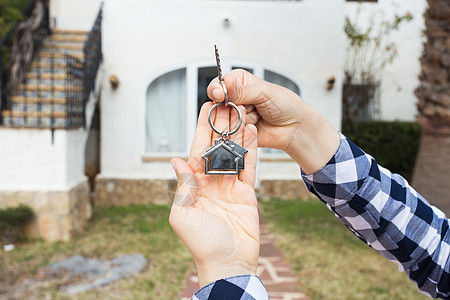 手持钥匙和以房子形状的钥匙链 新家背景的房屋钥匙 Home key建筑经纪人展示租户投资代理人钥匙圈住宅戒指女士图片
