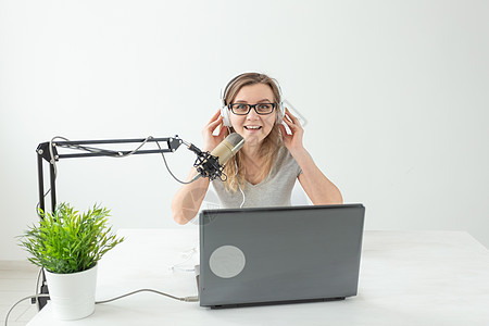 耳机包装电台主持人概念  在演播室的白色背景下 担任电台主持人的女性坐在麦克风前笔记本车站微笑植物扬声器电脑工作渠道广播耳机背景