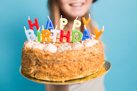 戴着眼镜和贺卡帽的漂亮女孩 手握着一个快乐的生日蛋糕 站在蓝背景上站着 她举起手来蛋糕情绪装饰庆典纪念日风格礼物潮人问候语海报图片