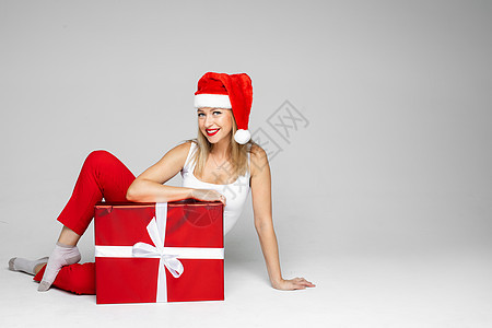 穿着圣诞帽子的小丑女人 坐在一个大红盒子里 照片在白色背景上被孤立庆典快乐季节性女性女孩微笑幸福新年红色女士图片