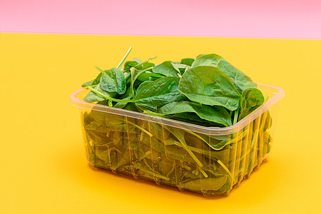 黄色背景透明塑料套件中新鲜的婴儿菠菜叶新片减肥饮食蔬菜排毒树叶食物植物活食生食沙拉图片