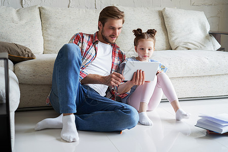 父亲和女儿坐在起居室的地板上 带着数字平板电脑微笑 教课图片