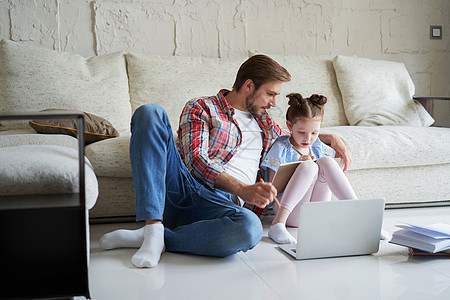 在客厅用笔记本电脑和教学课坐在地板上 父亲和女儿在微笑父母设备男人成人数字身份爸爸情感童年家庭图片