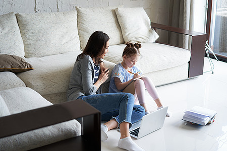 母亲和女儿在客厅用笔记本电脑坐在地板上微笑 教课图片