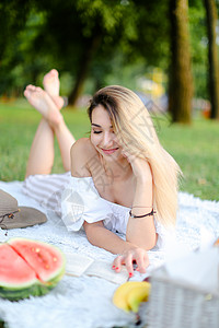 年轻快乐的女人躺在公园和阅读书上的格子上图片