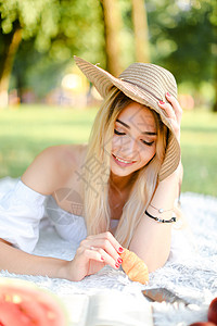 戴帽子的年轻caucasian女孩躺在公园里 坐在格子上 用智能手机冲浪图片