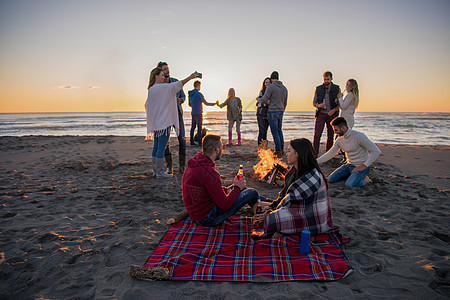 在海滩日落时和朋友共度欢乐的情侣友谊沙滩派对啤酒潮人营火场景男人城市假期图片