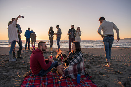 在海滩日落时和朋友共度欢乐的情侣啤酒火焰营火旅行城市幸福衣服场景假期乐趣图片