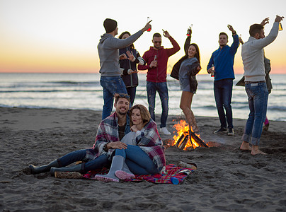 在海滩日落时和朋友共度欢乐的情侣火焰沙滩啤酒女性城市潮人旅行夫妻衣服友谊图片