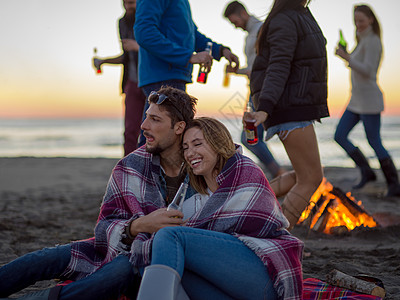 在海滩日落时和朋友共度欢乐的情侣场景旅行派对潮人友谊女性休闲篝火营火衣服图片
