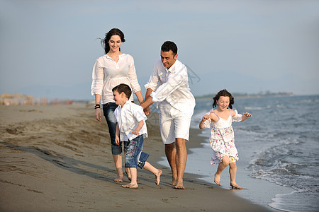 快乐的年轻家庭在海滩上玩得开心假期旅行女孩海洋父母女儿父亲天空儿子成人图片