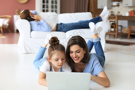 快乐的母亲和小女孩女孩在看笔记本电脑 与网络摄像头交谈 通过计算机应用程序在线聊天女儿用户家庭妈妈孩子们科技保姆讲话视频沙发背景图片