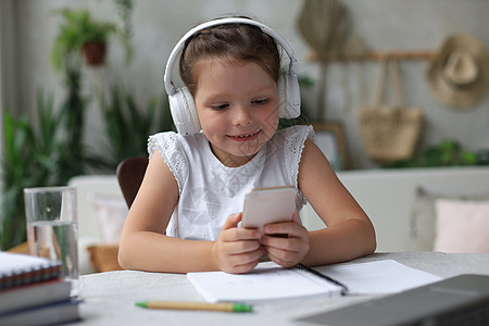 书本小素材戴耳机的聪明小女孩在智能手机上做家庭作业在线课程 戴耳机的小孩在互联网上学习 在隔离期间举行网络会议或上课白人屏幕教育微笑居家瞳背景