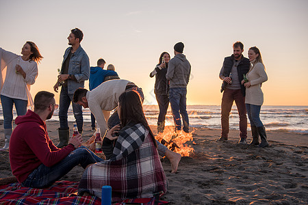在海滩日落时和朋友共度欢乐的情侣女性假期衣服友谊享受活动火焰朋友们营火潮人图片