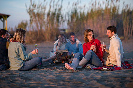 在海滩日落时和朋友共度欢乐的情侣城市火焰女性潮人假期友谊场景夫妻衣服啤酒图片