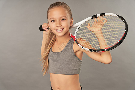 在灰色背景下站着网球拍的可爱女孩图片