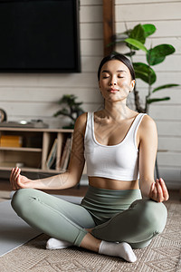 正念和冥想的概念 在家锻炼的亚洲年轻女性 在客厅的地垫上进行瑜伽冥想 变得专注技术成人重量运动装电脑女孩训练房间笔记本身体图片