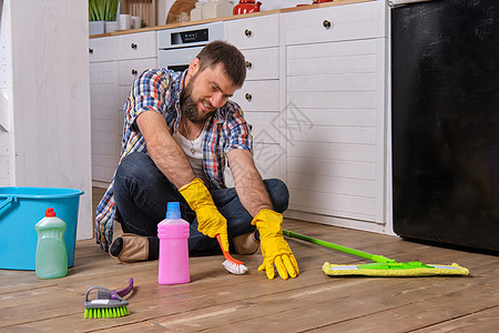 白种青年胡子男子坐在厨房的地板上 试图用他所有的洗涤剂 抹布 毛巾和刷子清洗干净清洁工男性补给品工作压力家务情感工具公寓男人图片